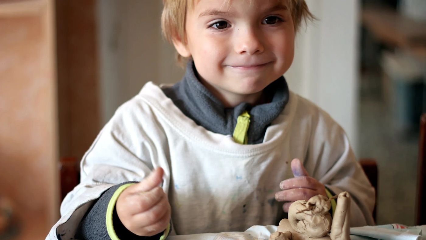 Uśmiechnięty chłopiec trzyma ceramiczną figurkę, którą wykonał